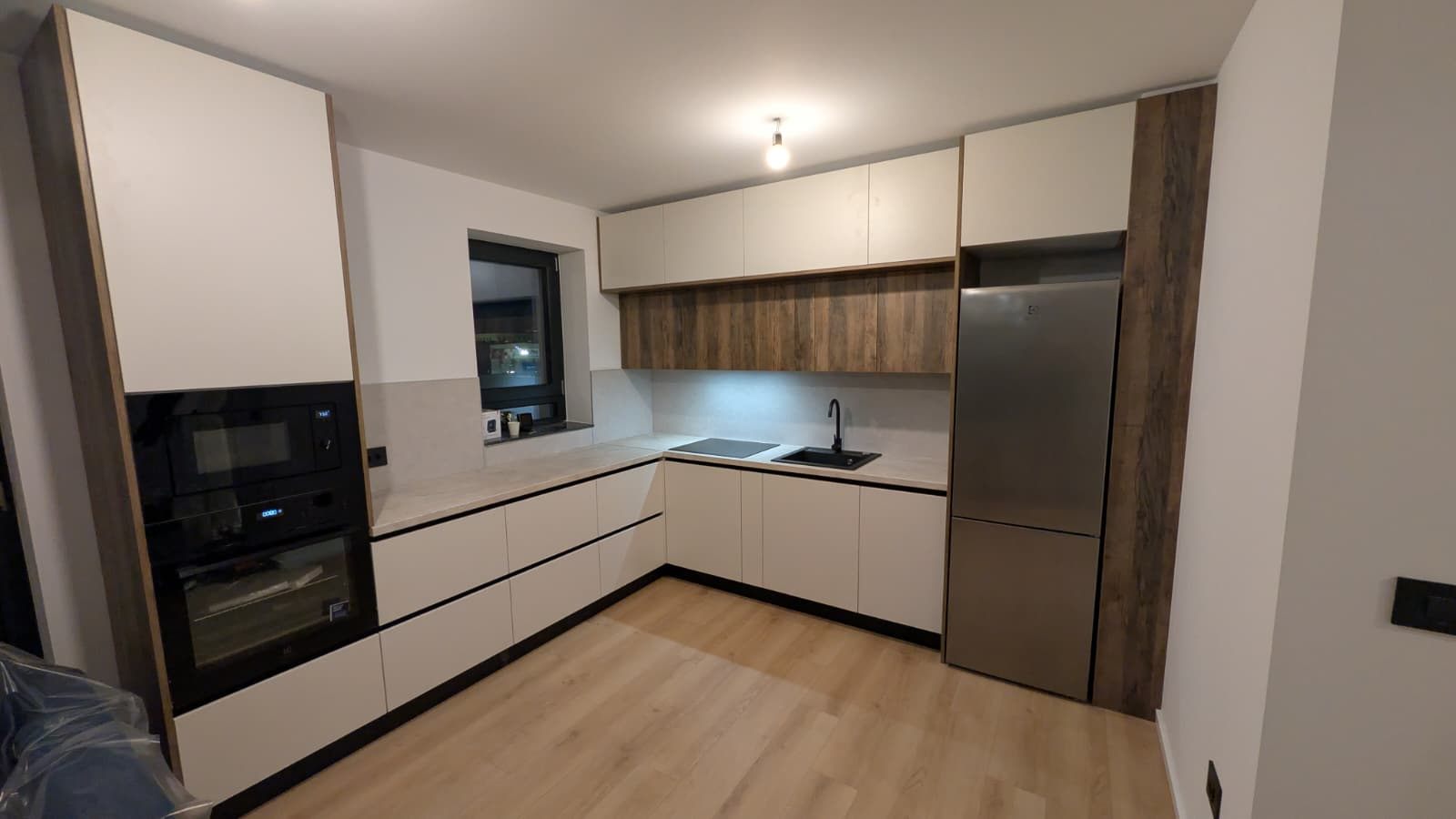 Bucătărie cu fronturi crem mate și frigider inox încadrat într-o coloană de nuc